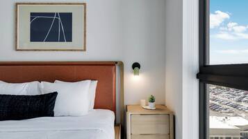 A hotel room with a bed, a nightstand with a lamp, a framed picture on the wall, and a window with a view of a parking lot.