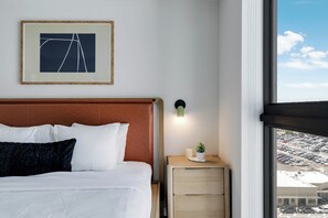 A hotel room with a bed, a nightstand with a lamp, a framed picture on the wall, and a window with a view of a parking lot. - Downtown Collective - Pool, Rooftop Bar (Miami)
