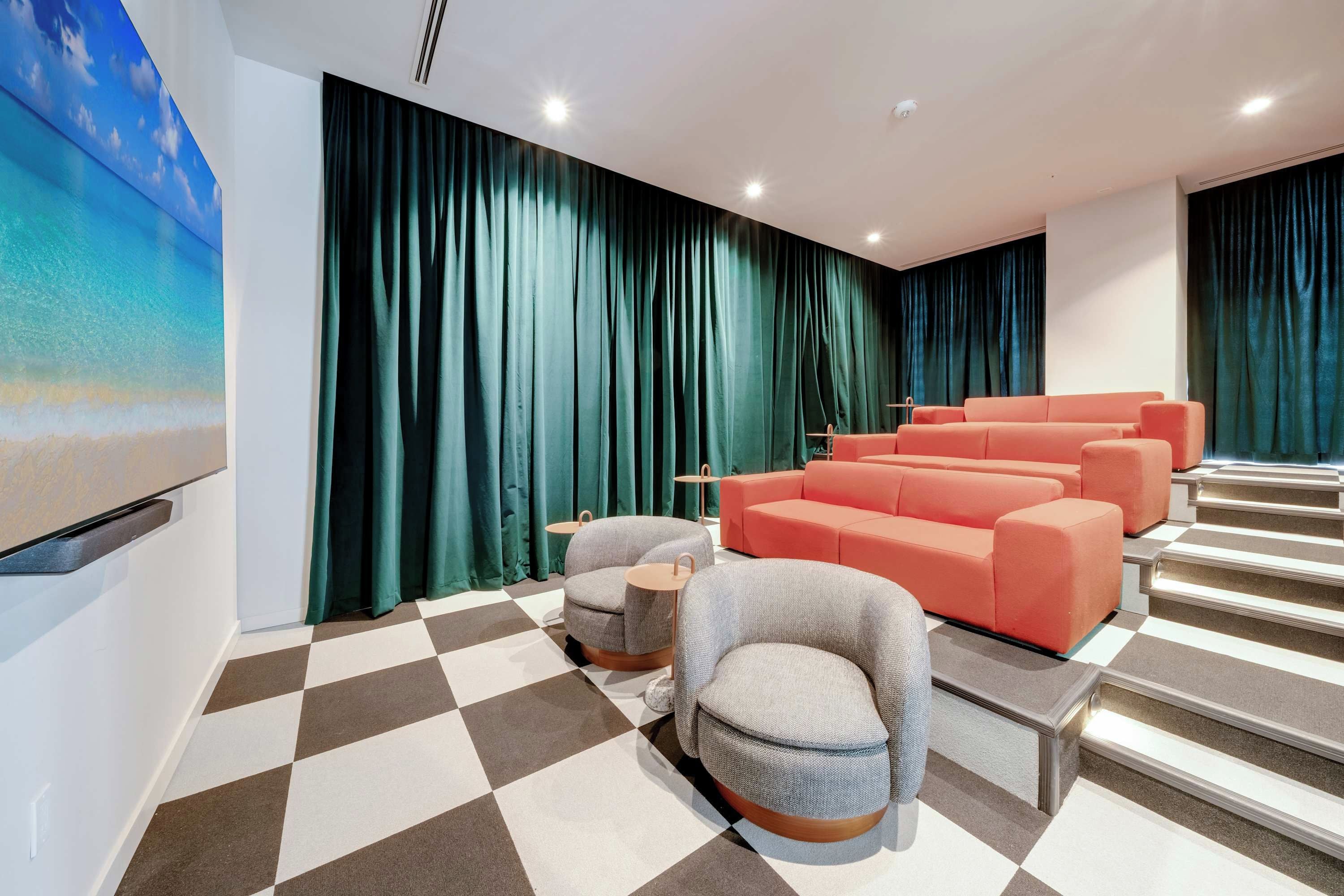 A modern cinema room with a checkered floor, grey and orange seating, and a large screen.