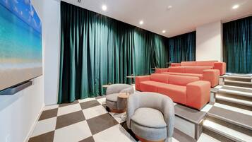A modern cinema room with a checkered floor, grey and orange seating, and a large screen.