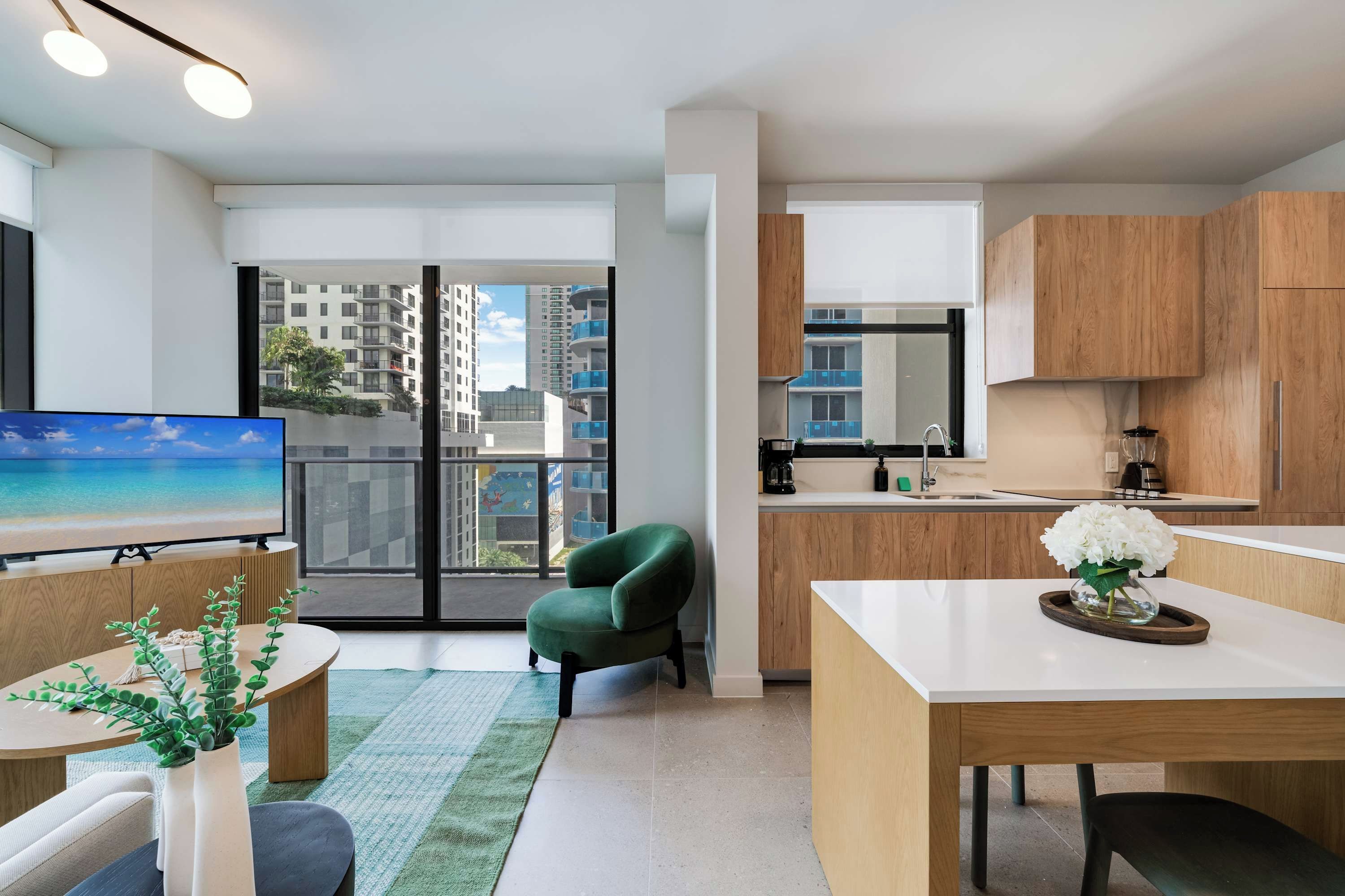 A modern apartment with a dining area, kitchen, and a balcony with a view of buildings.