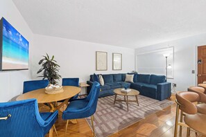 A modern living room with a blue sofa set, a wooden coffee table, and a dining table with chairs.