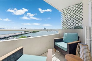 A balcony with a view of a river, a chair, a small table, and a patterned wall.