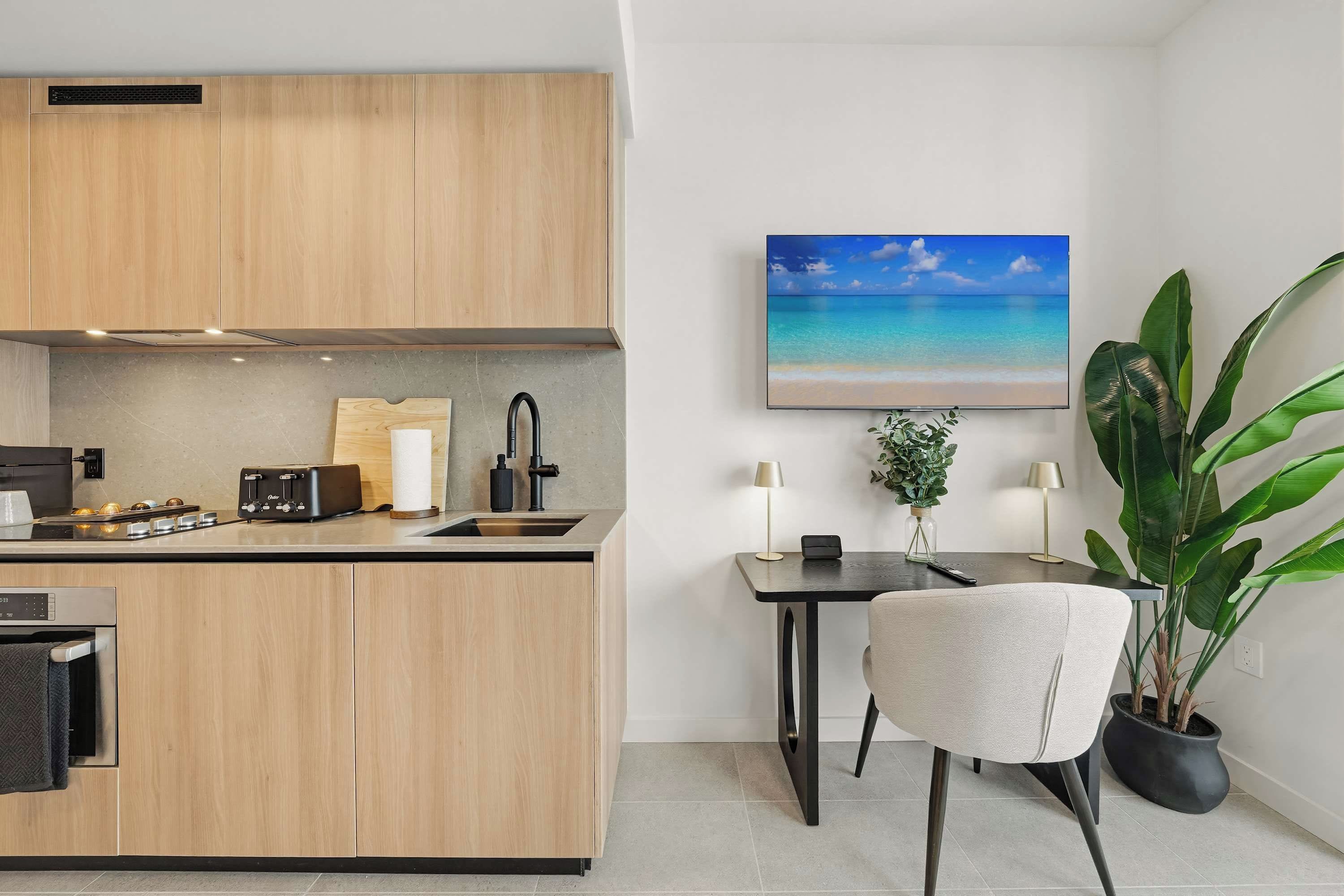 A modern kitchen with wooden cabinets, a countertop with a toaster, a sink, and a small dining area with a table and chair.