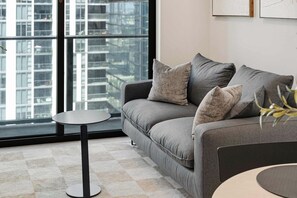 Ein modernes Wohnzimmer mit grauem Sofa, einem runden Beistelltisch und einem großen Fenster mit Blick auf die Stadt.