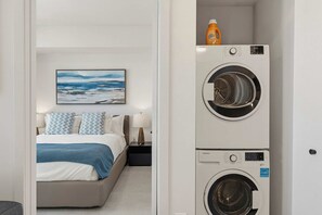Ein Hotelzimmer mit einem Bett, einem Nachttisch, einer Lampe, einem Gemälde und einem gestapelten Wascher und Trockner.