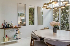 Un área de comedor moderna con una mesa redonda, sillas y un carrito bar con botellas.
