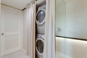 A laundry room with two stacked washing machines, a door with a window, and a glass partition. - Casa Anton Artist Home, Pool & Rooftop Terrace (Miami)