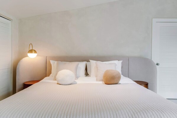 A neatly made bed with a textured white duvet, two fluffy pillows, and a bedside lamp on a wooden nightstand.