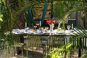 An outdoor dining area with a table set for four, surrounded by green chairs, with a grill and plants in the background. - Casa Anton Artist Home, Pool & Rooftop Terrace (Miami)