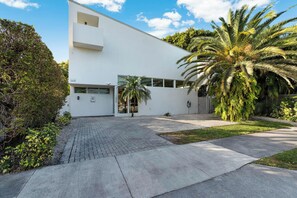 A modern white building with a flat roof, a paved driveway, and a palm tree in the foreground.