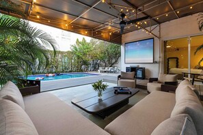 A modern outdoor lounge area with a pool, comfortable seating, and a projector screen.