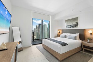 Quarto de hotel moderno com uma cama grande, uma escrivaninha, uma cadeira e vista para a paisagem urbana pela varanda.