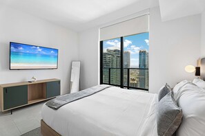 Quarto moderno com cama, televisão, mesa de cabeceira e uma grande janela com vista para a cidade.