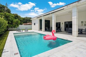 Ein Swimmingpool mit einem rosa Flamingo-Schwimmtier, umgeben von einer überdachten Terrasse mit Stühlen und Tischen.