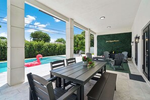 Ein überdachter Außenbereich mit Pool, Sitzgelegenheiten und einer grünen Wand mit einem Zitat.