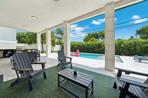 Ein überdachter Außenbereich mit Sitzgelegenheiten, einem Pool und Blick auf die umliegende Grünfläche.