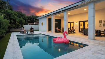 A swimming pool with a pink flamingo float, surrounded by a covered patio area with seating.
