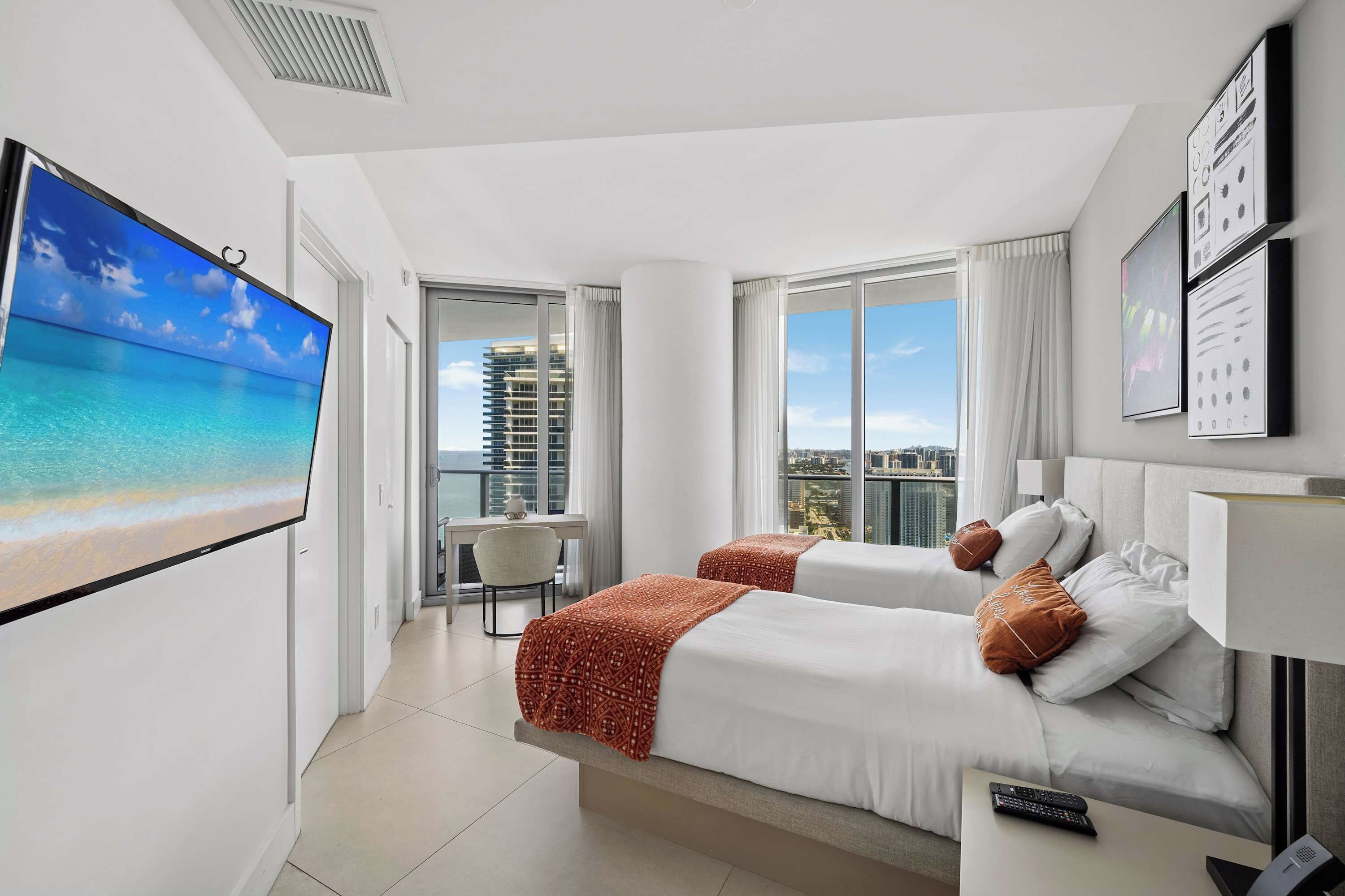 A hotel room with two beds, a TV, a desk, and a view of the city.