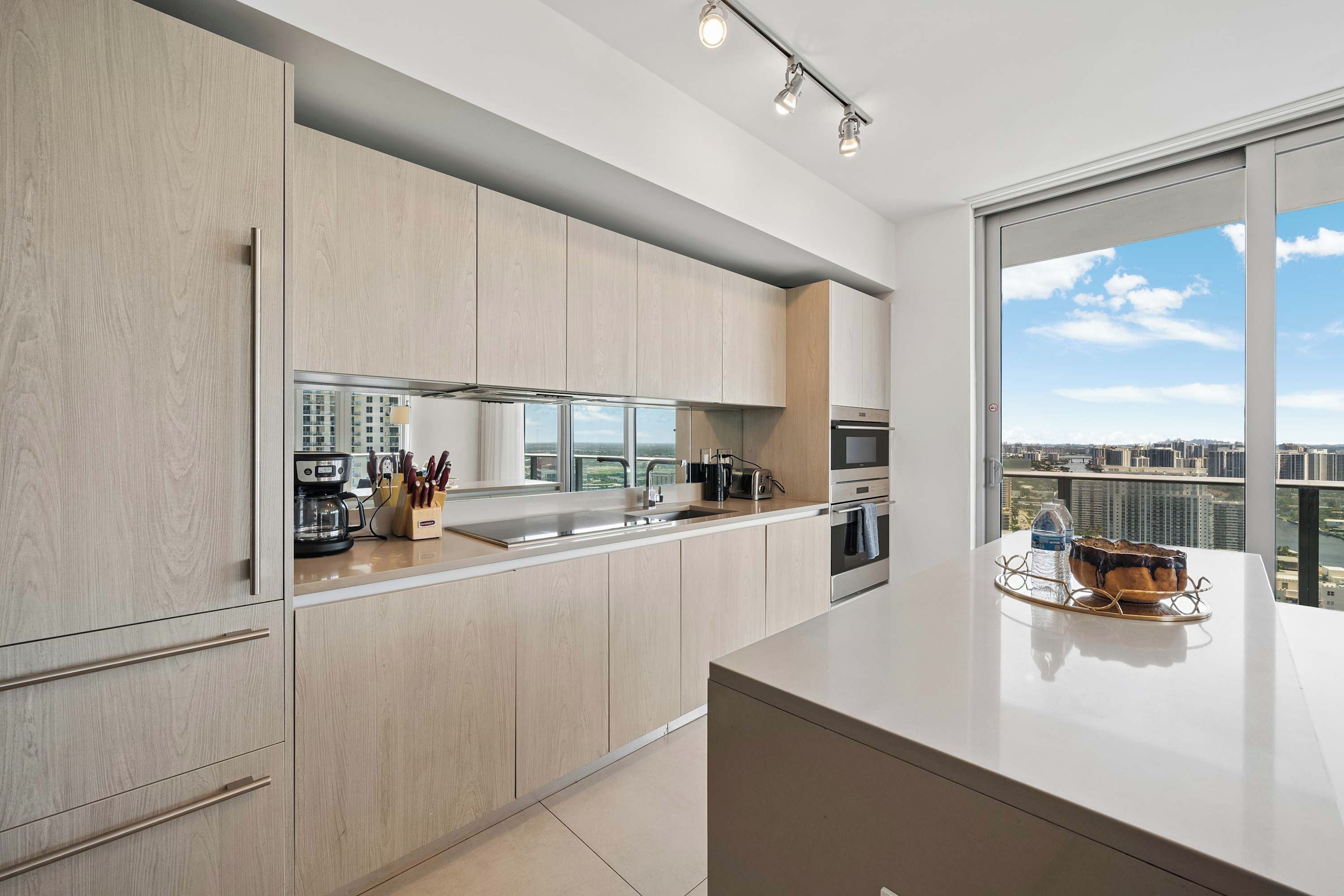 A modern kitchen with a large window, a coffee machine, and a view of the city.