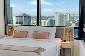 A hotel room with a large bed, two bedside tables, a nightstand, and a view of the cityscape through large windows. - Sky Corner Residence Pool, Parking, Amenities (Miami)