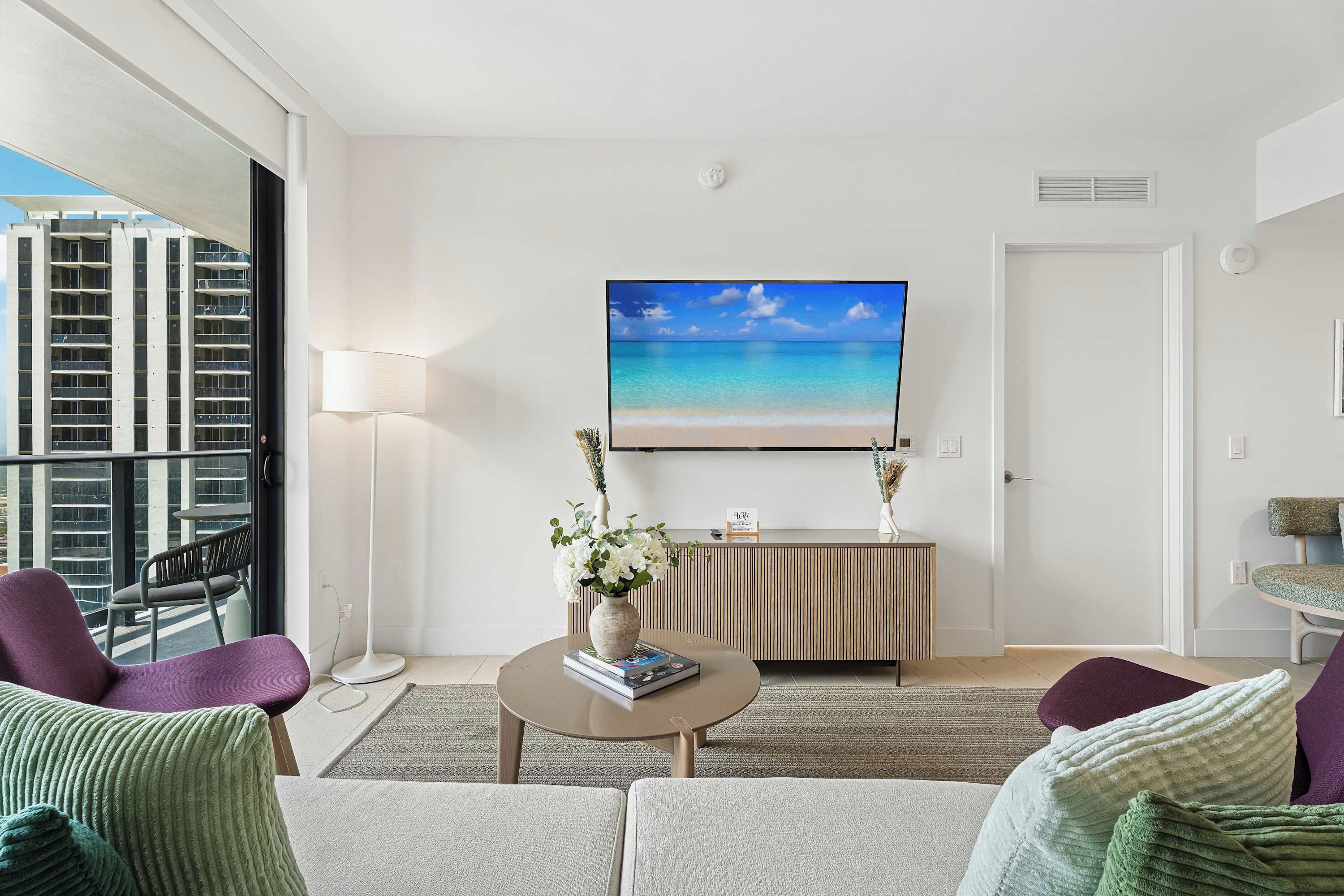 A modern living room with a large TV, a sofa, a coffee table, and a view of a building outside.