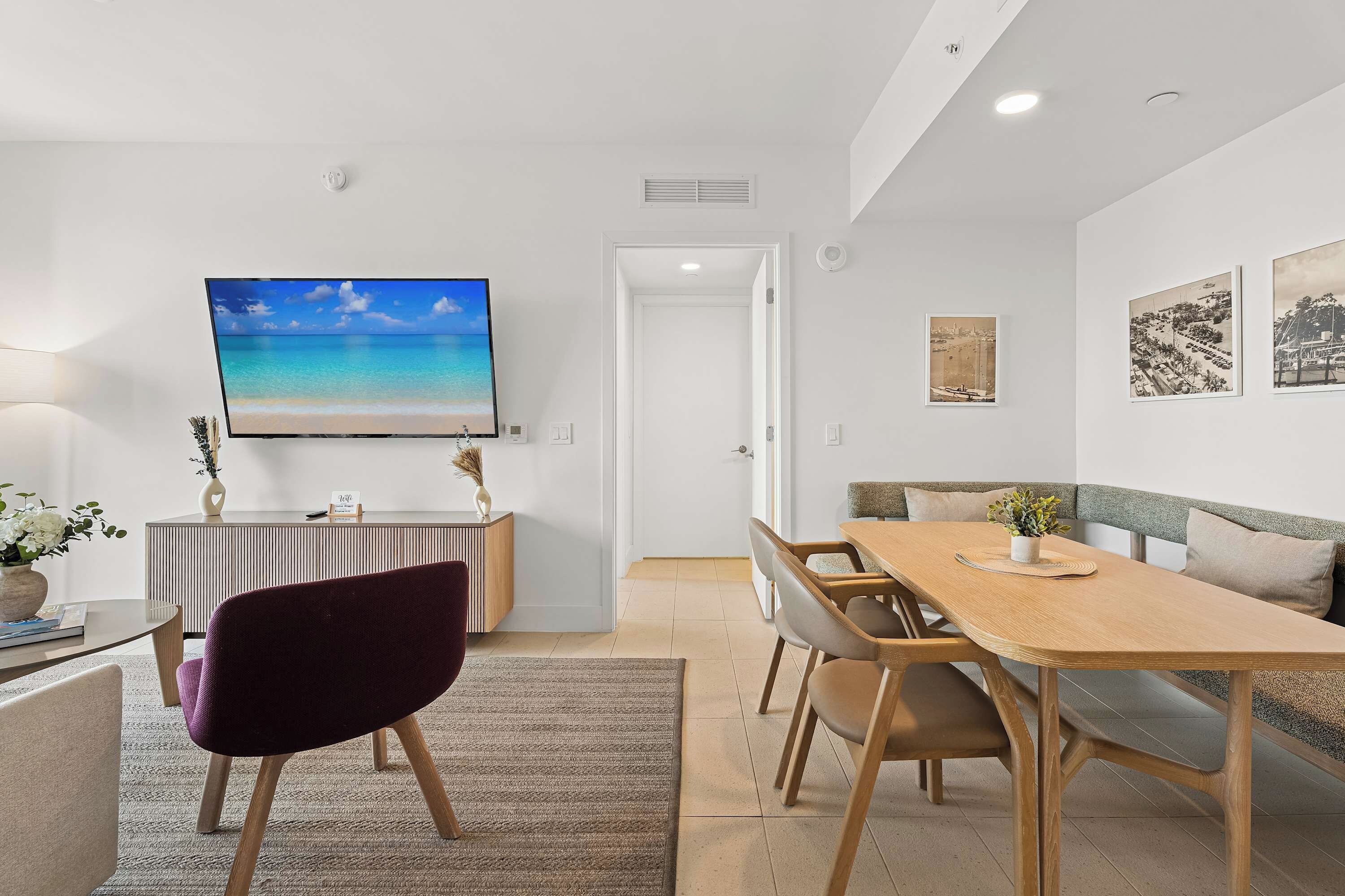 Un'area pranzo moderna con un tavolo e sedie in legno, una TV a schermo piatto montata a parete e un piccolo tavolino con un vaso.