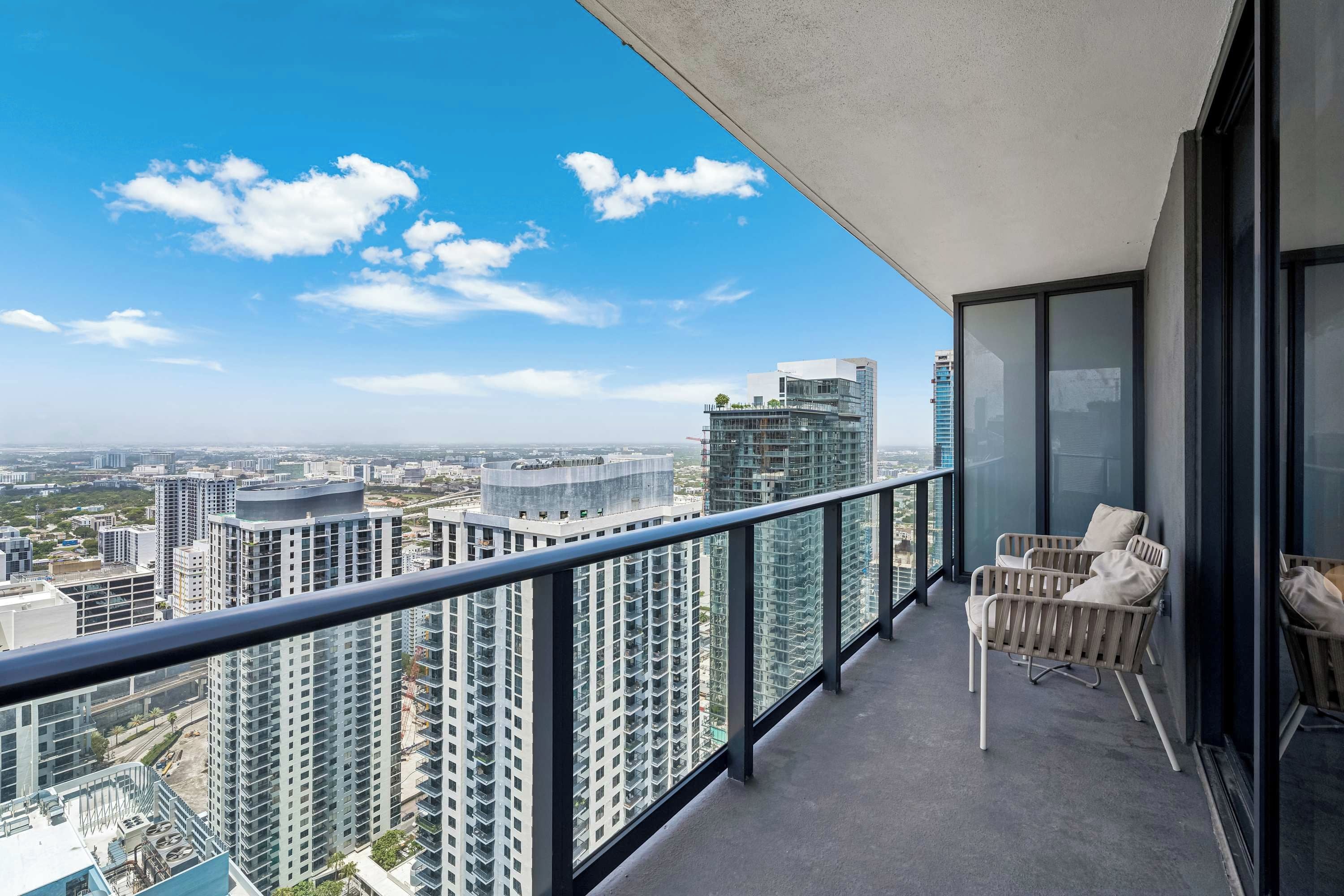 Ein Balkon mit Blick auf hohe Gebäude, einer Glasumlaufung und zwei Korbstühle.