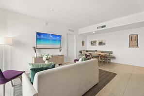 Ein modernes Wohnzimmer mit Fernseher, einer Couch, einem Essbereich mit Tisch und Stühlen sowie einem Wandbild.