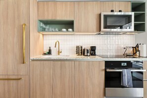 Eine moderne Küche mit Holzausstattung, einem Edelstahlbackofen, einer Mikrowelle und einer Kaffeemaschine.