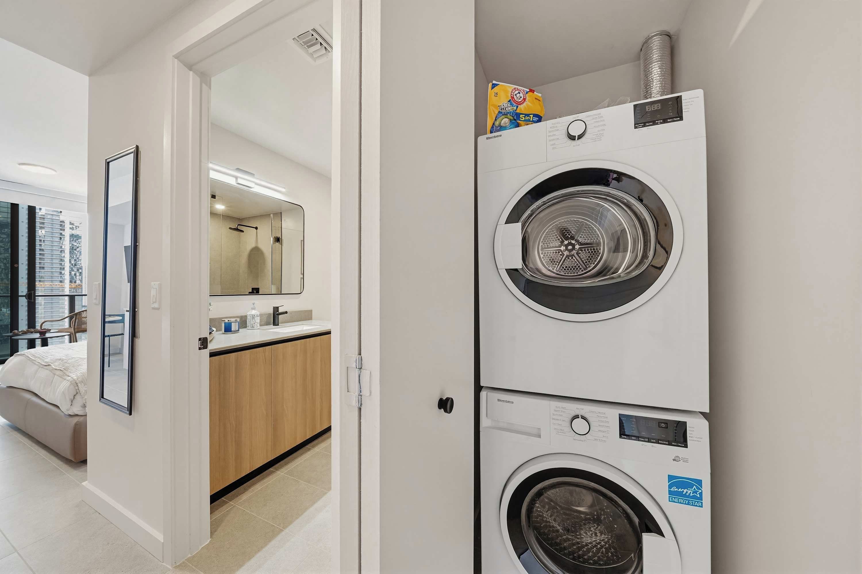 Una habitación de hotel moderna con cama, un baño con espejo y una lavadora y secadora apiladas.
