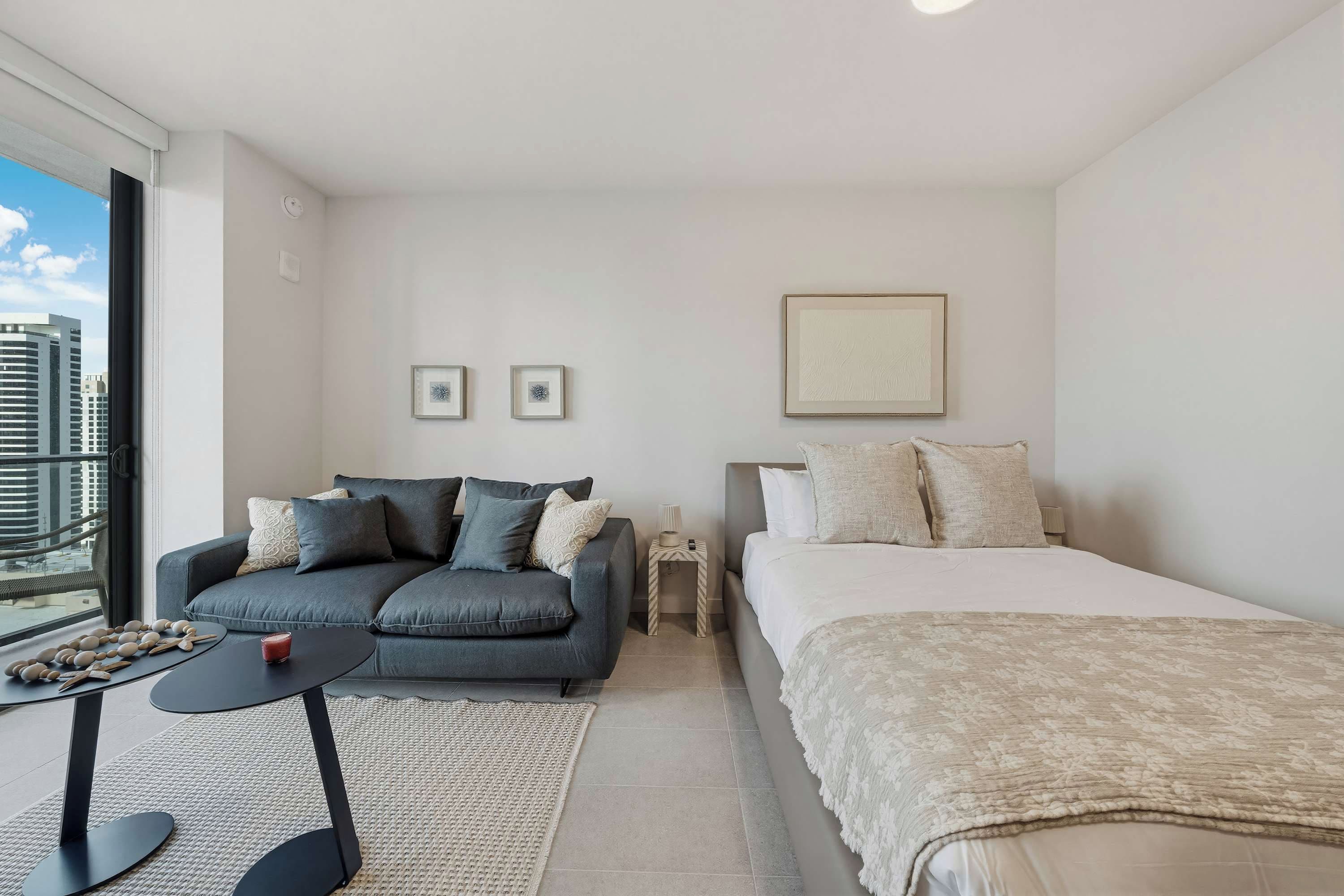 Ein modernes Hotelzimmer mit Sofa, Bett, einem kleinen Tisch und Blick auf die Stadt.