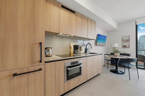 A modern kitchen with wooden cabinets, a built-in oven, a coffee maker, and a dining area with a table and chairs. - Cielo Studio Downtown Location and City Views (Miami)