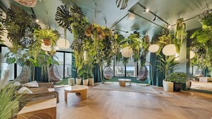 Een ruime kamer met een houten vloer, hangplanten en een groot raam met uitzicht op de stad.