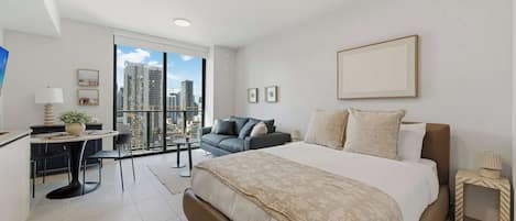 A modern hotel room with a large bed, a desk, a sofa, and a view of the cityscape.