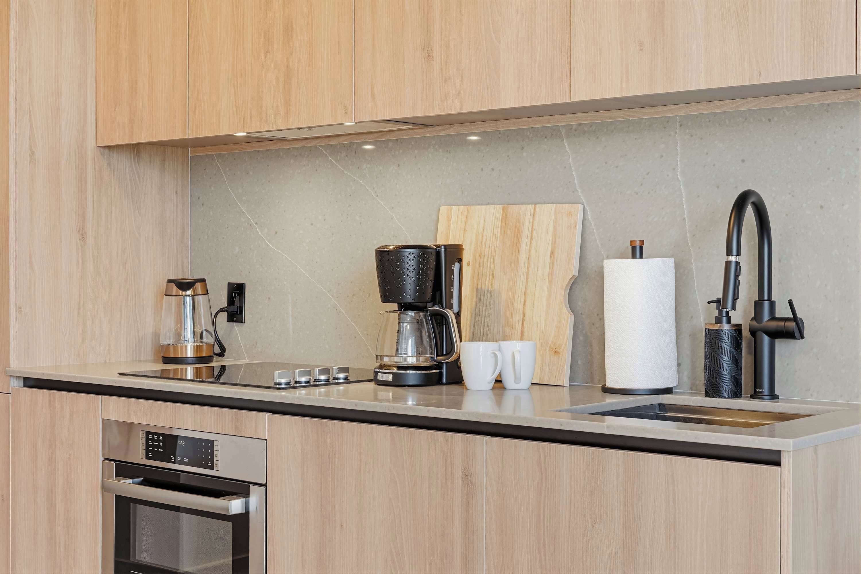 Una cocina moderna con horno integrado, cafetera, hervidor y dispensador de toallas de papel.