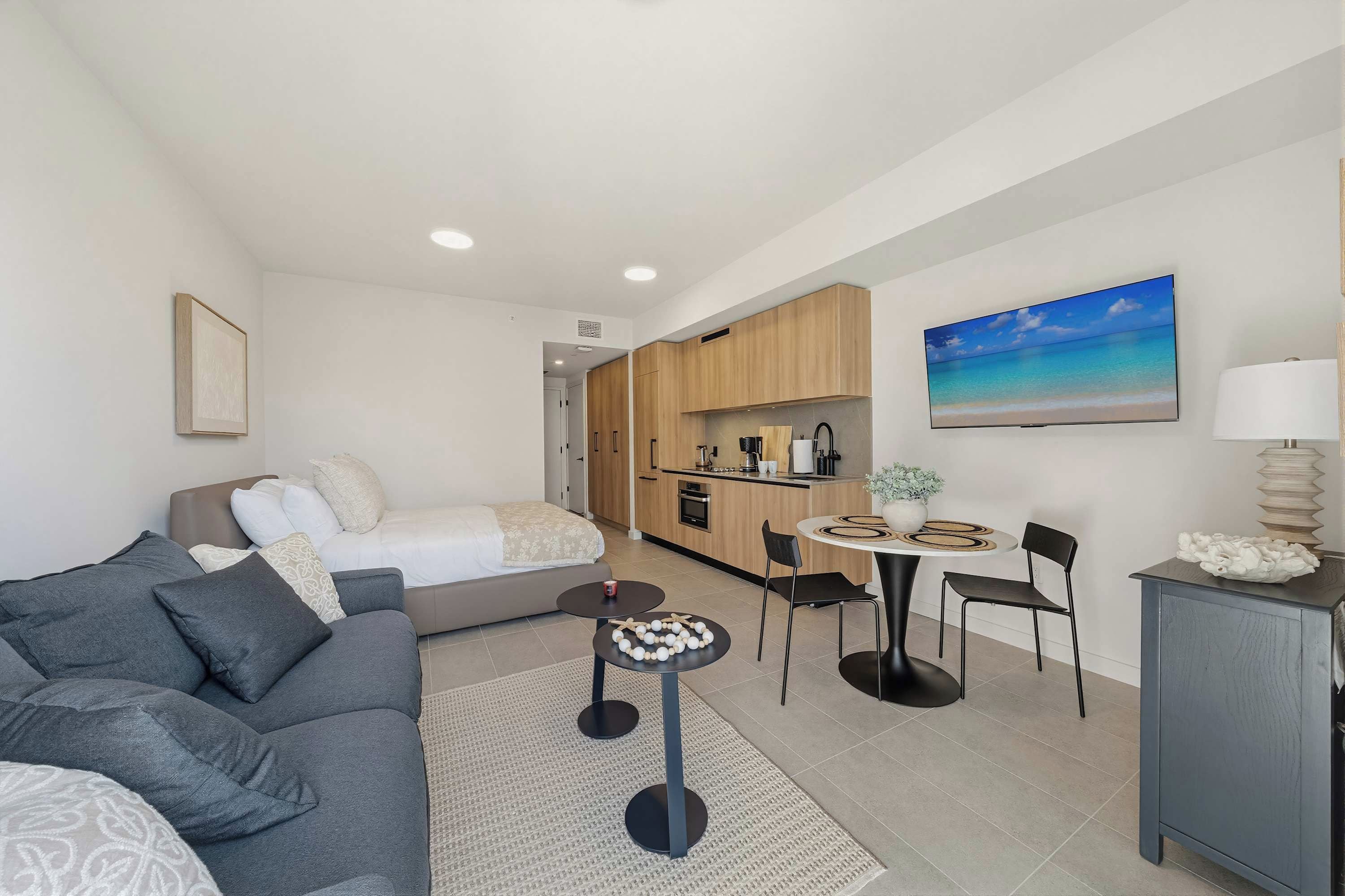 A modern apartment with a living area, kitchenette, dining table, and a painting of a beach.
