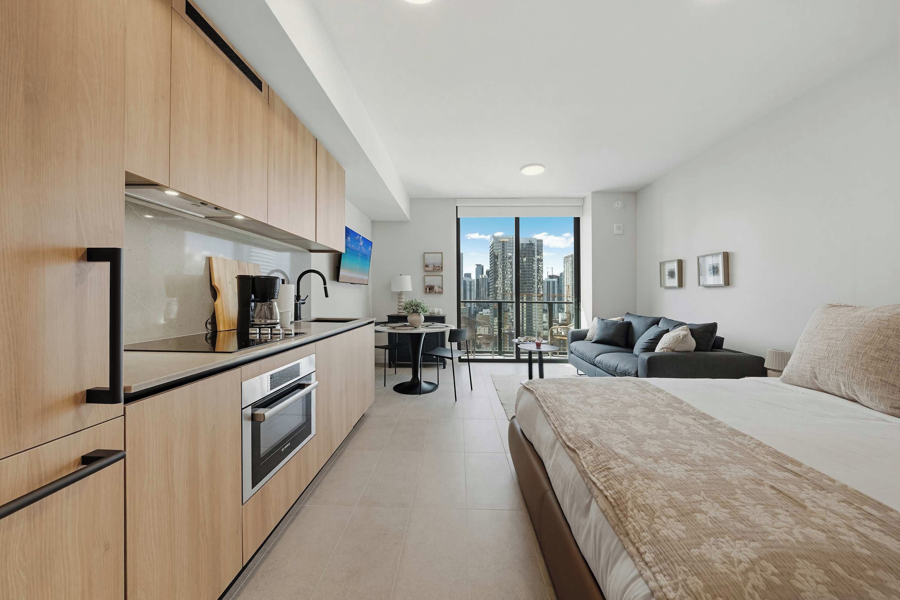 Une chambre d’hôtel moderne équipée d’une kitchenette, d’un lit, d’un canapé et d’une grande fenêtre donnant sur la ville.