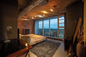 Une chambre avec une grande fenêtre, un lit, un bureau et une chaise.