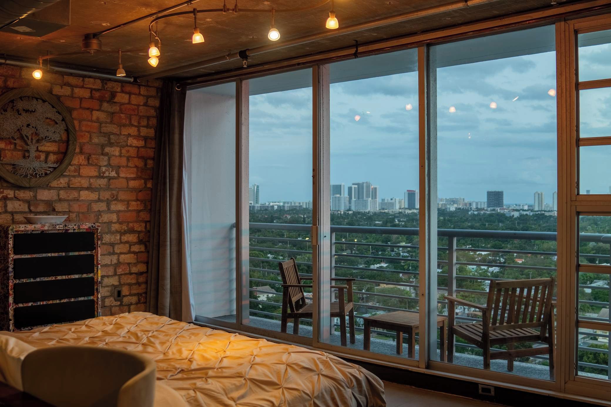 Un dormitorio con un ventanal grande, una cama, una silla de madera y una mesita.