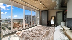 A bedroom with a large bed, a view of the city, and a balcony with chairs. - Hollywood Beach Speakeasy Condo With Pool (Hollywood)