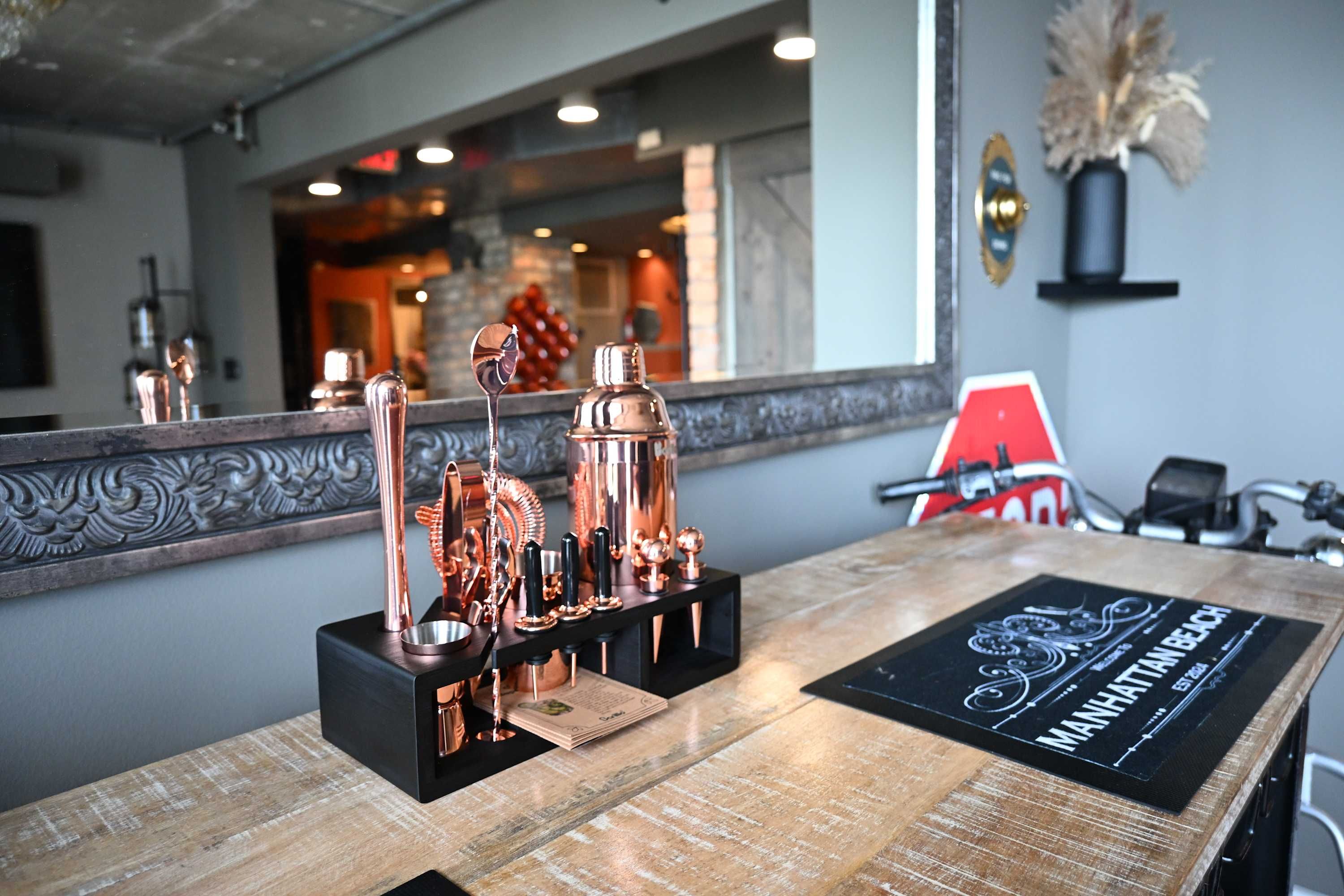 Uma área de bar com utensílios de cobre e um porta-copos preto com o texto 'Manhattan Beach'.