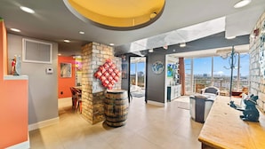 A spacious room with a large window, a wooden bar, and a stone wall. - Hollywood Beach Speakeasy Condo With Pool (Hollywood)