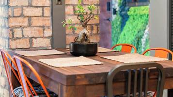 Ein Holztisch mit Bonsai-Baum als Mittelpunkt, umgeben von orangefarbenen Stühlen mit gestreiften Kissen.