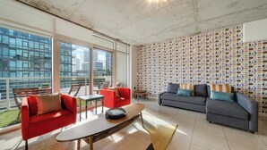 A spacious living area with large windows, a red and grey sofa set, a coffee table, and a patterned wall. - Midtown Rouge- Condo With City Views, Pool & Gym (Miami)