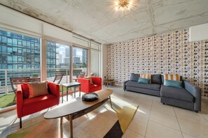 A spacious living area with large windows, a red and grey sofa set, a coffee table, and a patterned wall. - Midtown Rouge- Condo With City Views, Pool & Gym (Miami)