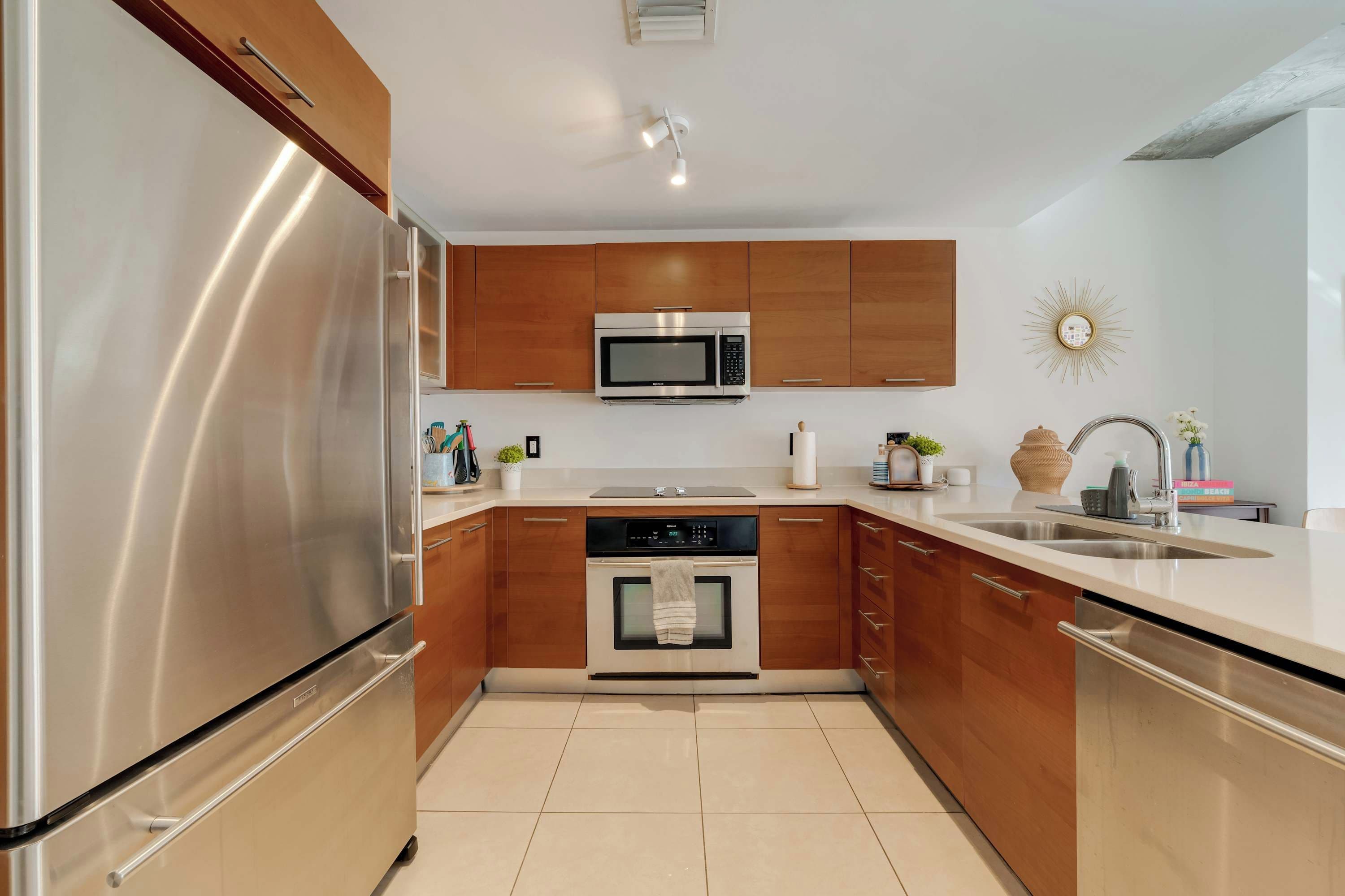 Uma cozinha moderna com eletrodomésticos de aço inoxidável, armários de madeira e bancada branca.