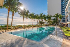 A swimming pool with a view of the ocean, surrounded by palm trees and lounge chairs. - Sea Escape- Private Sun Deck, Beachfront and Views (Miami Beach)