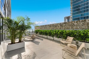 A rooftop terrace with lounge chairs, potted plants, and a view of a cityscape. - Sea Escape- Private Sun Deck, Beachfront and Views (Miami Beach)
