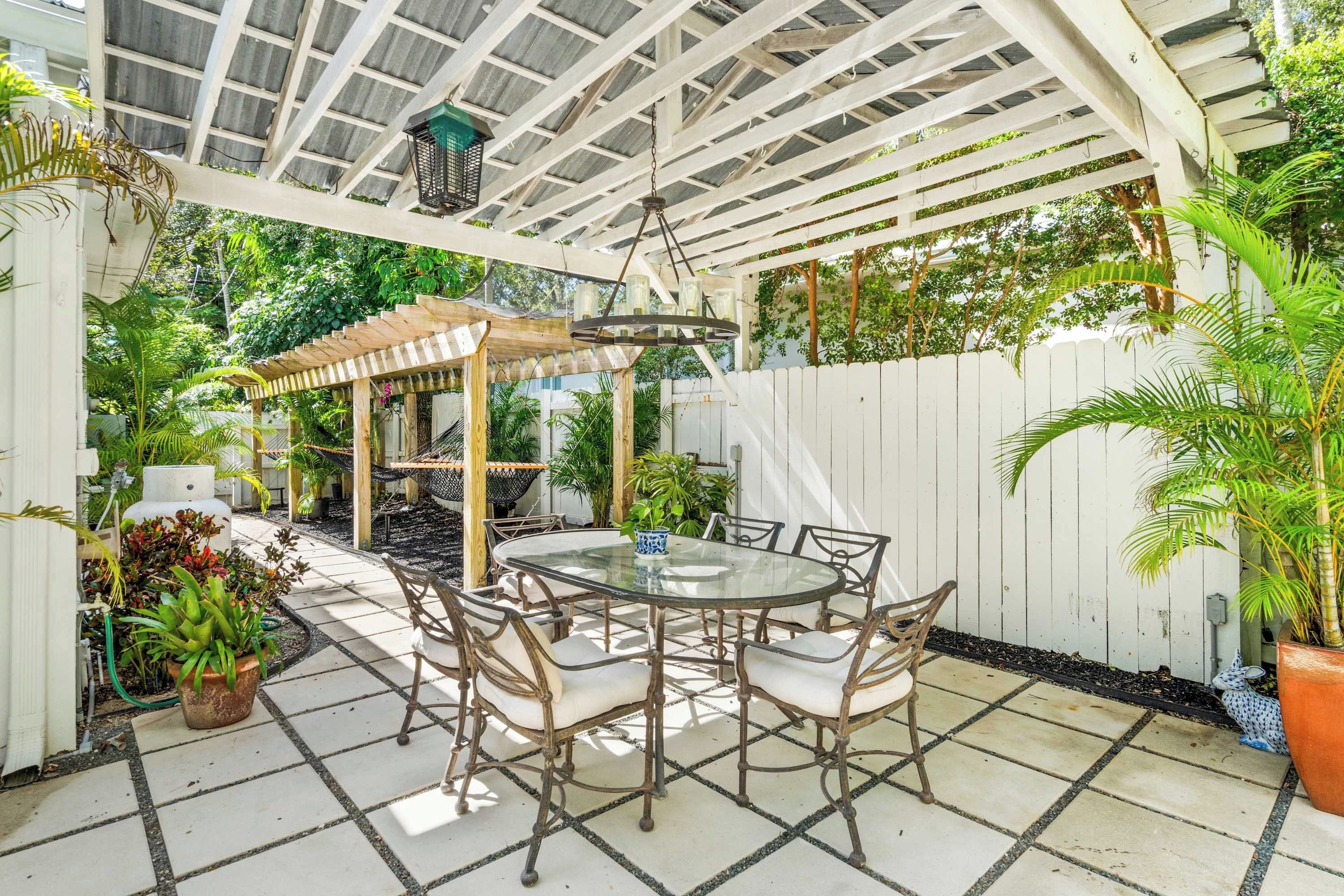 Eine überdachte Terrasse mit einem runden Tisch und Stühlen, umgeben von Blumentöpfen und einer Pergola.